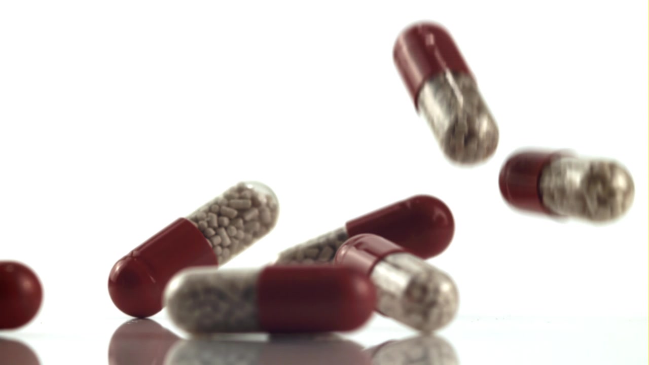 Capsule rosse e trasparenti che cadono su una superficie bianca.