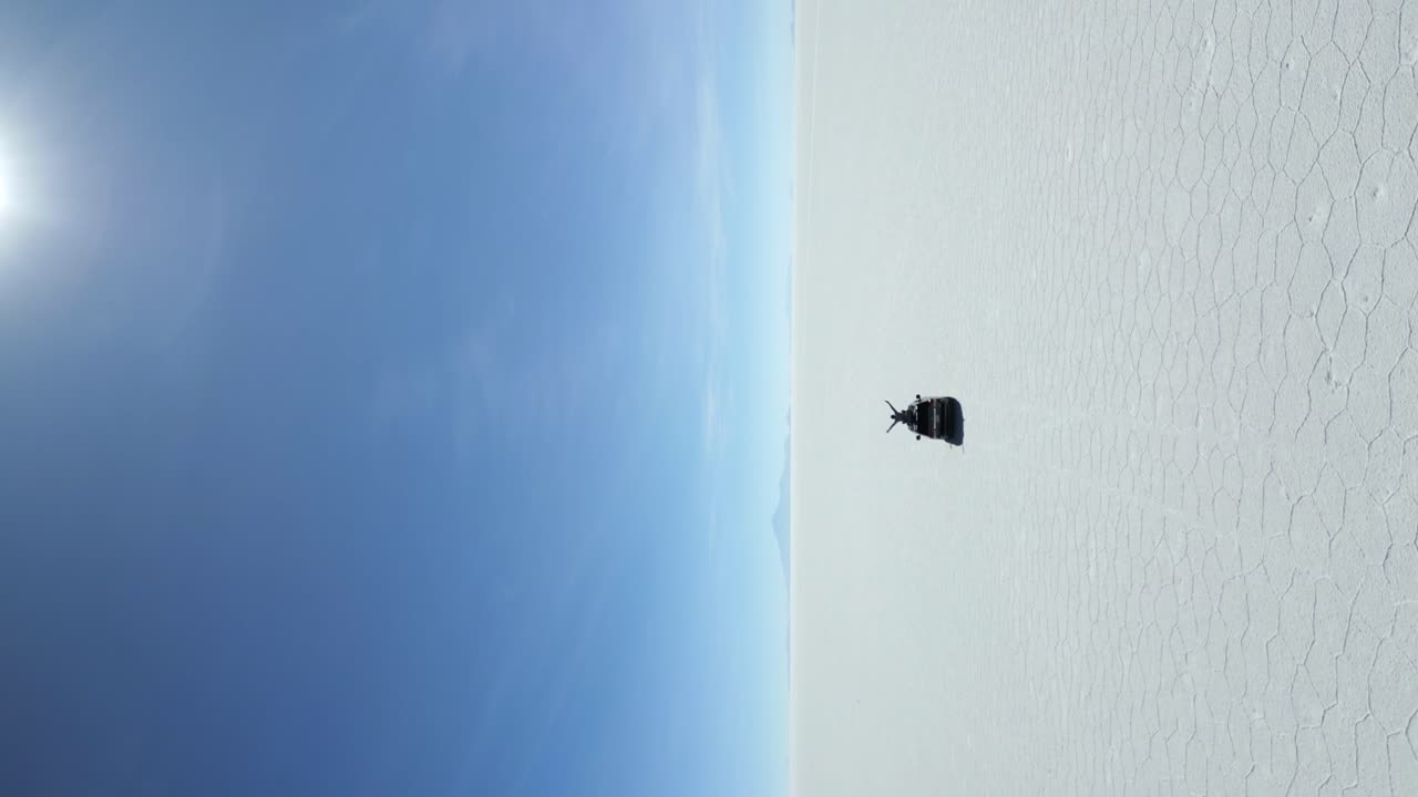 salar de uyuni를 가로질러 운전하는 차와 함께 선루프에 있는 남자가 팔을 높이 들고, 공중 수직 추적