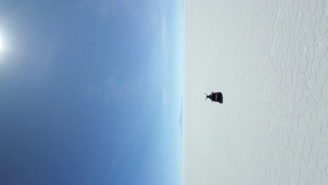 car driving across salar de uyuni with a man on sunroof raising his arms up high, aerial vertical tracking shot