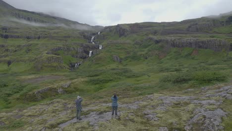 ascending aerial drone shot showing tourist visiting idyllic seven-tier waterfall in iceland - cinematic drone footage during cloudy day