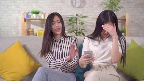 two young asian women saw the shocking content on their smartphone while sitting on the sofa in the living room