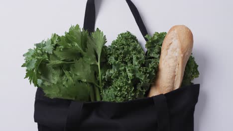 Video-of-black-canvas-bag-with-parsley,-kale-and-baguette,-copy-space-on-white-background