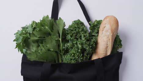 video de una bolsa de lienzo negro con perejil, col rizada y baguette, copia espacio en fondo blanco