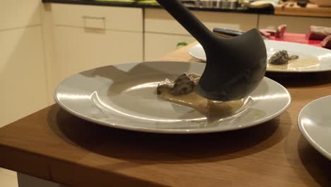 a white hand model is preparing morel sauce on a white plate with a black ladle