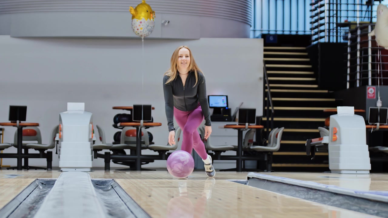 Una giocatrice sta ferma cercando di lanciare una palla da bowling viola lungo la pista liscia.