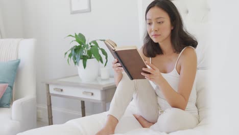 happy asian woman sitting on bed and reading book, in slow motion