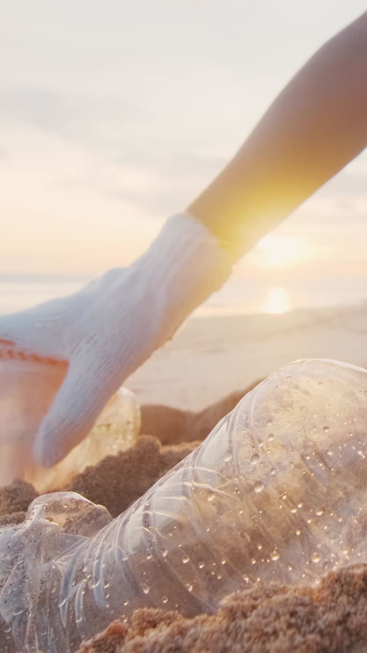Hands of environmental activist collecting garbage and bottles from sandy beach