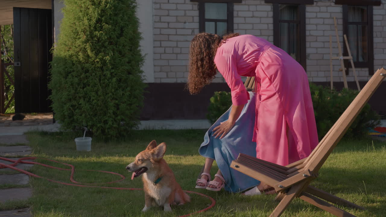 Child With Dog, Young Girl Enjoying Sunny Outdoor Scene, Child Resting On Outdoor Chair With Furry Friend Nearby, Young Girl Sitting Peacefully On Patio With Corgi And Family Surroundings