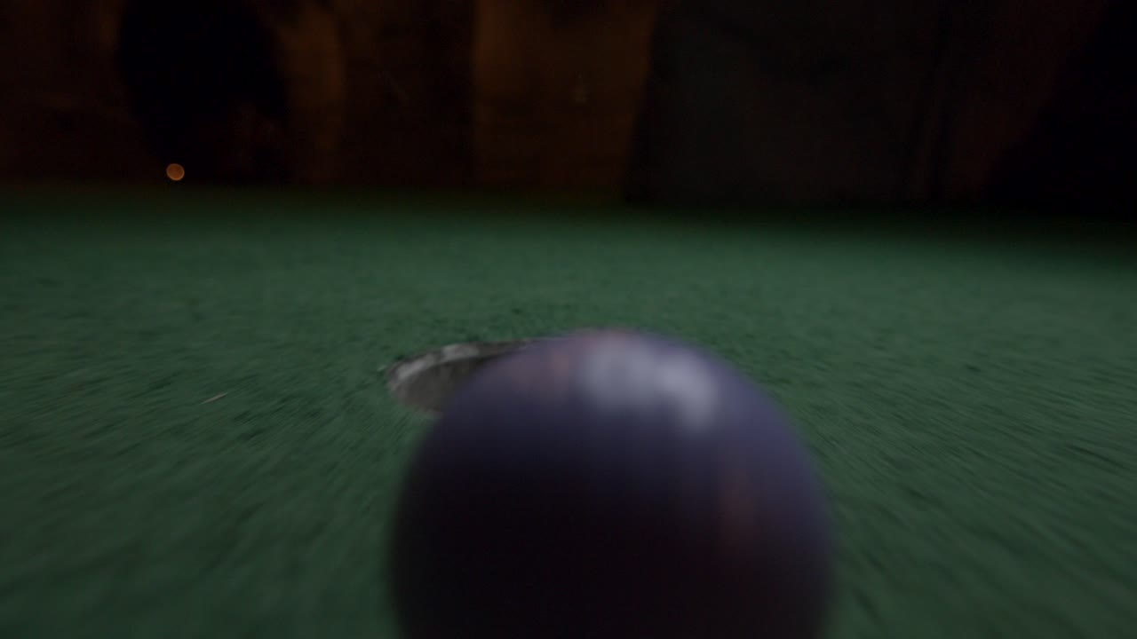 Una pallina da minigolf viola cade nella buca e rimbalza nel raccoglitore su un campo da gioco.