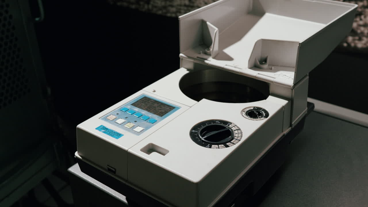 Close-up of a coin counting machine placed on a desk, turned off and unused, in a typical office or bank setting.