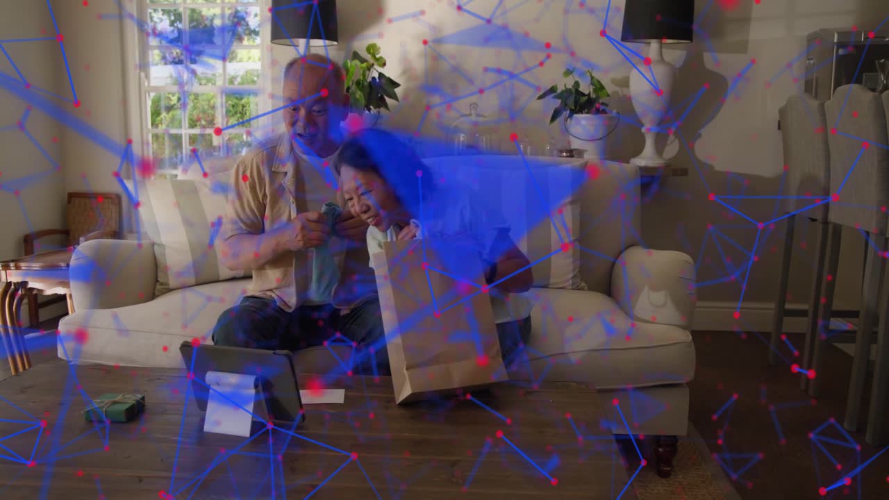 Mature couple reaching bag on sofa, showing blue item to tablet for web feedback, overlay appearing