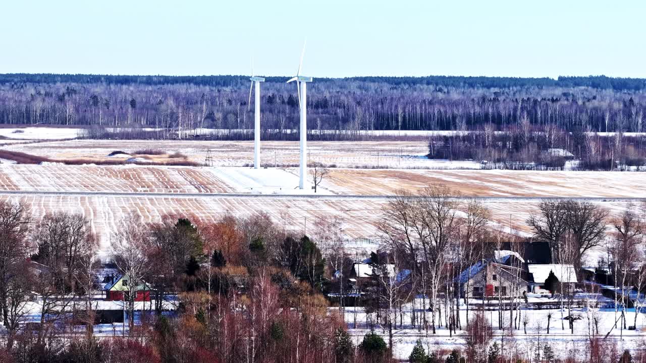 Turbine eoliche che generano energia pulita su campi innevati e una foresta distante.