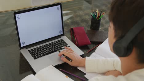 Asian-male-teenager-with-headphones-learning-and-using-laptop-in-living-room