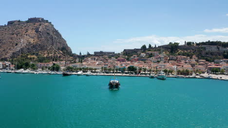 old wooden boat leaving at nafplio port with fortress of palamidi in the background in greece