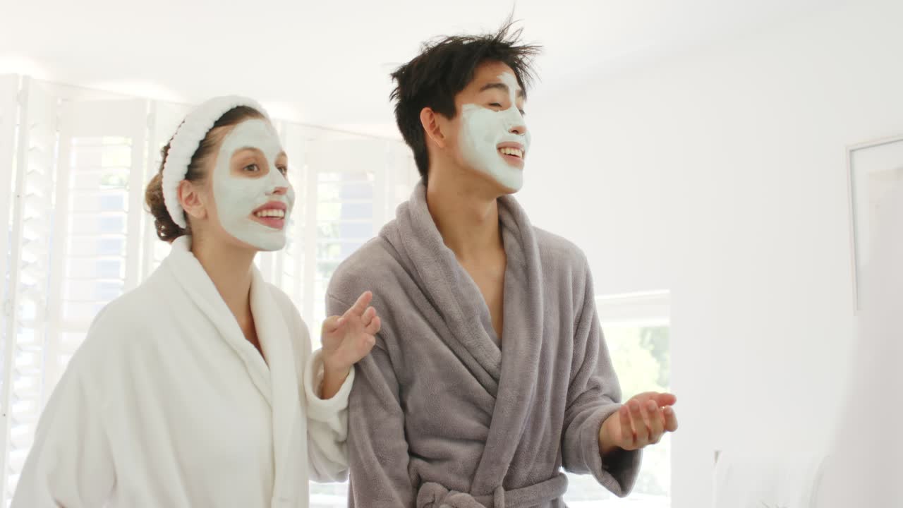 After mask application Asian man and African American woman wearing robes gesturing inspecting skin