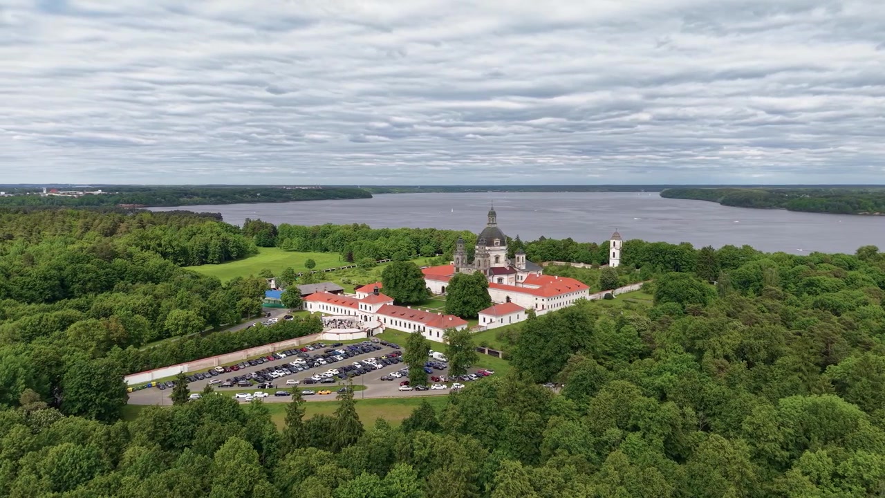 Splendido video con drone che riprende lo storico Monastero di Pazaislis circondato da fitte foreste verdi, auto parcheggiate e un sereno lago sotto cieli drammatici e coperti a Kaunas, Lituania