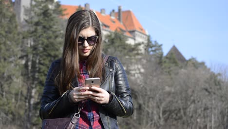 niña de cabello castaño enviando mensajes a su teléfono en un parque público en un hermoso día soleado
