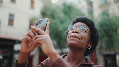mujer bonita con gafas con teléfono celular sonriendo en la calle
