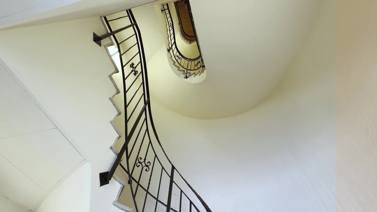 Una luminosa scala a chiocciola in marmo è ripresa dalle scale, guardando verso i piani superiori. Curve eleganti, ringhiera decorativa in ferro battuto. Inquadratura dal basso verso l'alto dall'interno della scala