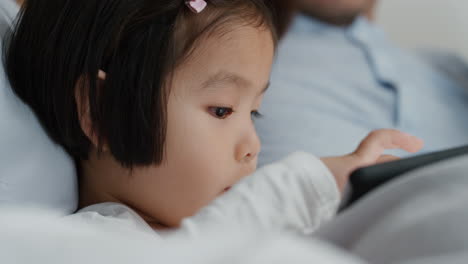 Linda-Niña-Asiática-Usando-Una-Tableta-Con-Su-Familia-Disfrutando-Jugando-Juegos-En-Un-Dispositivo-De-Pantalla-Táctil-Relajándose-Juntos-En-Casa-4k