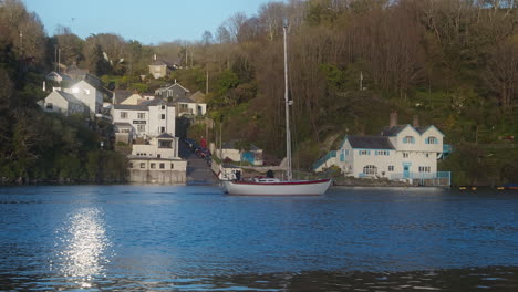 zeilboot vaart door glinsterende fowey rivier, cornwall met historisch daphne du maurier huis op de achtergrond - breedbeeld