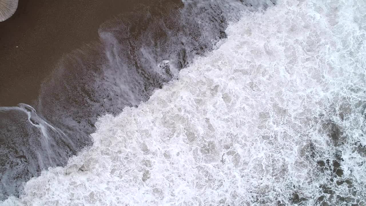 Aerial view of the waves, sandy beach with reed umbrellas