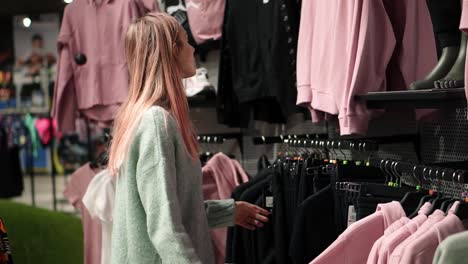 slender woman choosing clothes from rack in clothing store