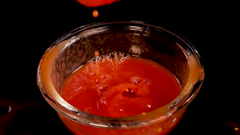 a whole tomato is dropped into a glass bowl filled with peeled tomatoes and sauce, creating a splash. shot in slow motion with dramatic lighting and a black background