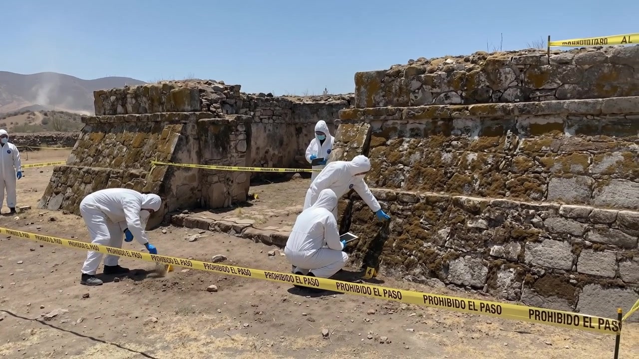 Equipe forense em trajes brancos de proteção investigando um local arqueológico ou cena de crime ao ar livre.