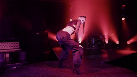 slow movement camera captures a dancer in black pants and a long braid dancing on stage, bathed in concert lighting