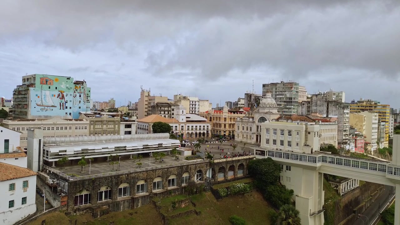 Zoom out aereo con drone che rivela l'Elevador Lacerda, la piazza del centro storico e i murales urbani colorati a Salvador, Bahia, Brasile.