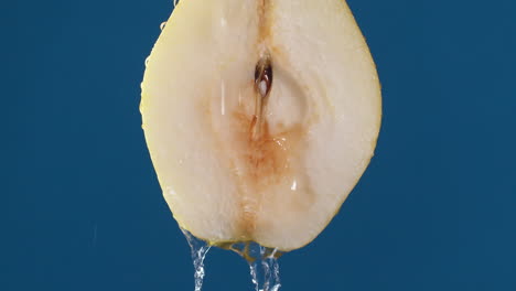 yellow half pear on a blue dark background with drops of water rolling down the pear and flowing splashing with isolated background