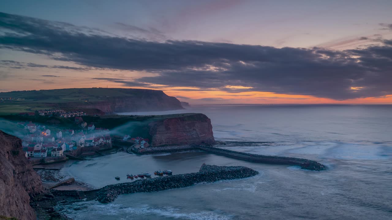 북 요크셔의 시 마을인 스테이스 (staithes) 에서 해가 지고 있으며, 항구는 절벽 속에 자리잡고 있다.