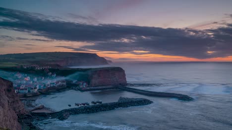 Puesta-De-Sol-Sobre-El-Pueblo-Pesquero-De-Staithes,-En-Yorkshire-Del-Norte,-Con-El-Puerto-Enclavado-Entre-Los-Acantilados.