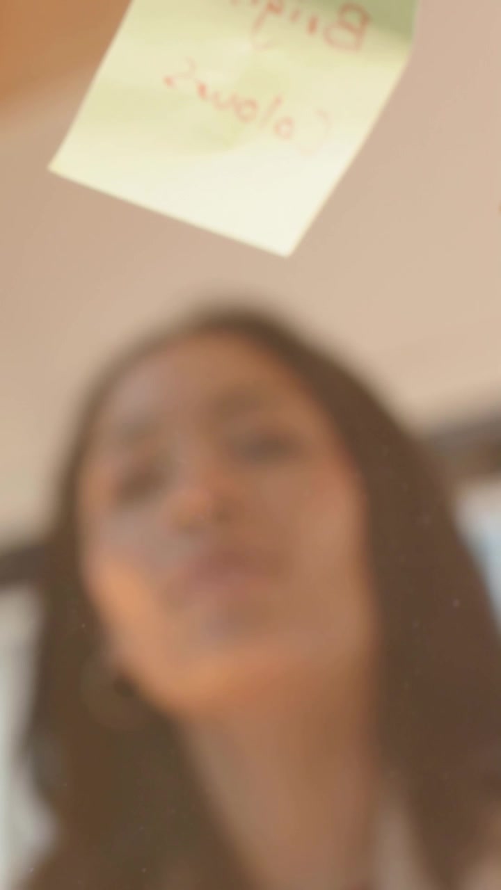 Vertical video: Marker entering woman leaning, adjusting note, writing on glass in room, copy space