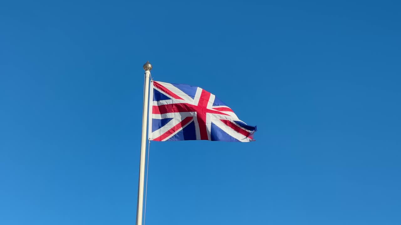 Union Jack British UK Flag Waving in the Wind Against Clear Blue Sky National Symbol Patriotism United Kingdom Banner