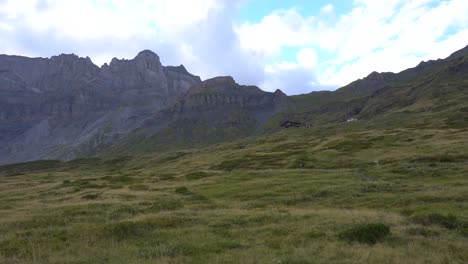 Hiker-Walking-Along-a-Path-towards-a-Mountain-Lodge-in-a-Vast-Alpine-Valley-surrounded-by-Rocky-Peaks