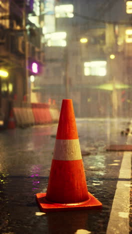 un cono de tráfico solitario se encuentra en el medio de una calle húmeda por la noche en una ciudad