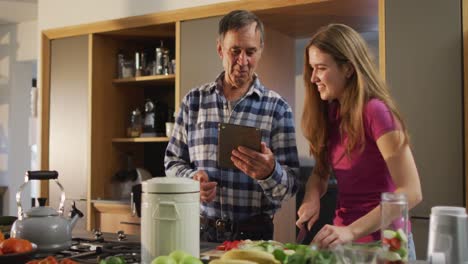 Smiling-caucasian-senior-father-with-teenage-daughter-preparing-food-and-using-tablet-in-kitchen