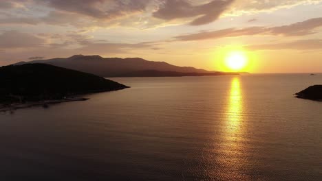 drone view in albania flying over blue crystal clear water on sunset, with the sun setting in the horizon with an island in ksamil