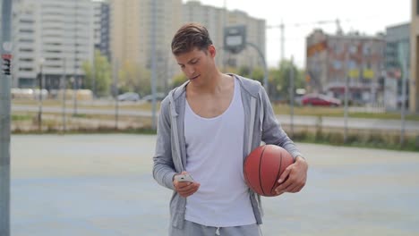 young attractive man with basketball looking attentively at screen of smartphone