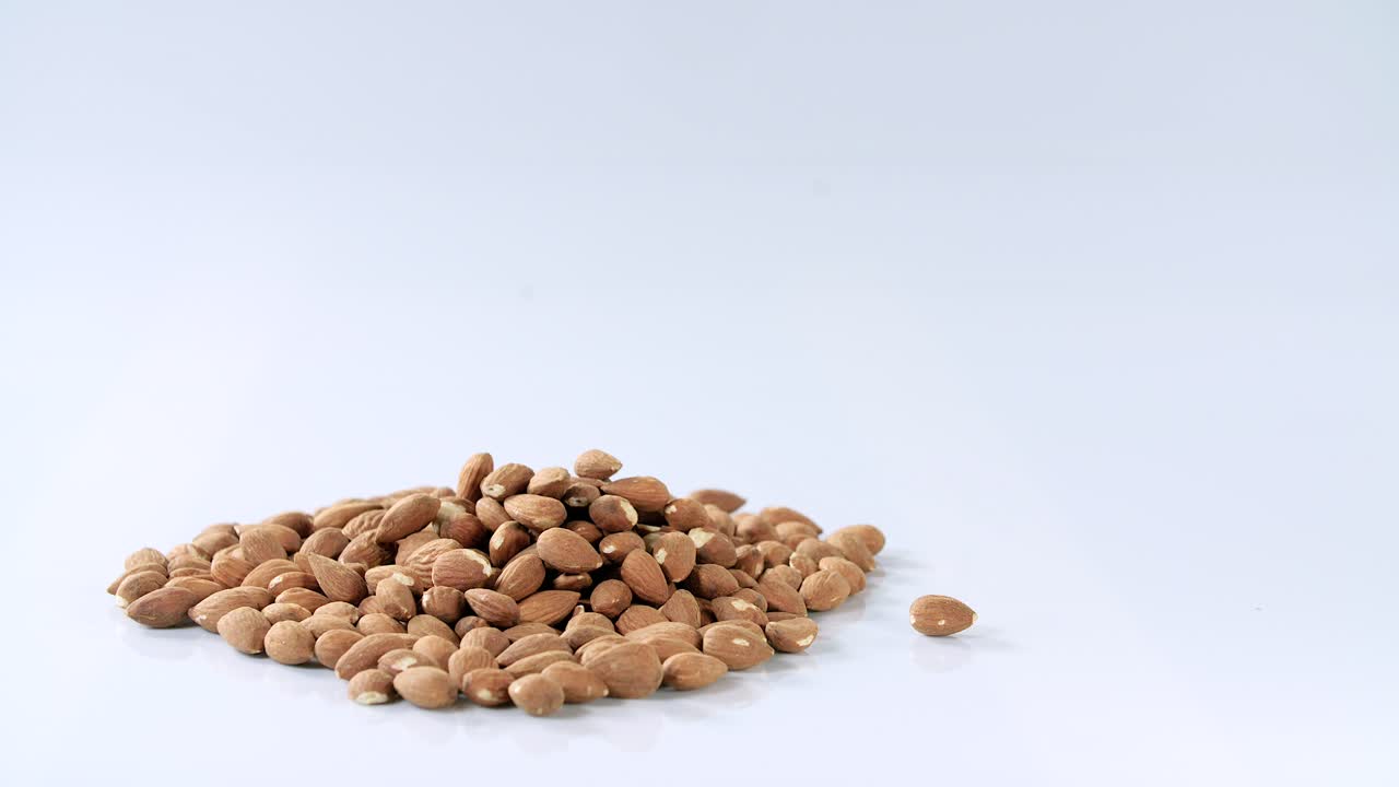 man drops a hand full of unroasted almonds on a pile, then grabs a hand full, white reflective background