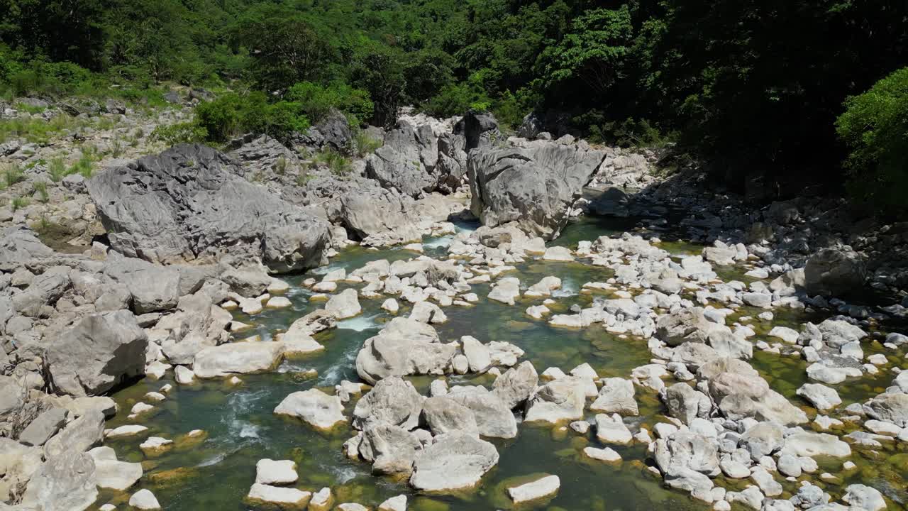 A low aerial shot tilts and moves sideways, revealing Tinipak River’s winding white rocks and lush greenery, capturing the natural beauty from a close, dynamic perspective
