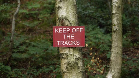 Keep-Off-The-Tracks-red-warning-sign-on-a-tree,-in-rural-Peak-District,-England,-in-4K