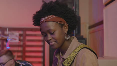 young girl playing guitar in recording studio while her friends discussing song together