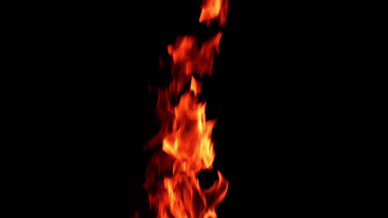 Long and thin flame of the fire burning in the darkness isolated. Tiny sparkles rise up in the air.