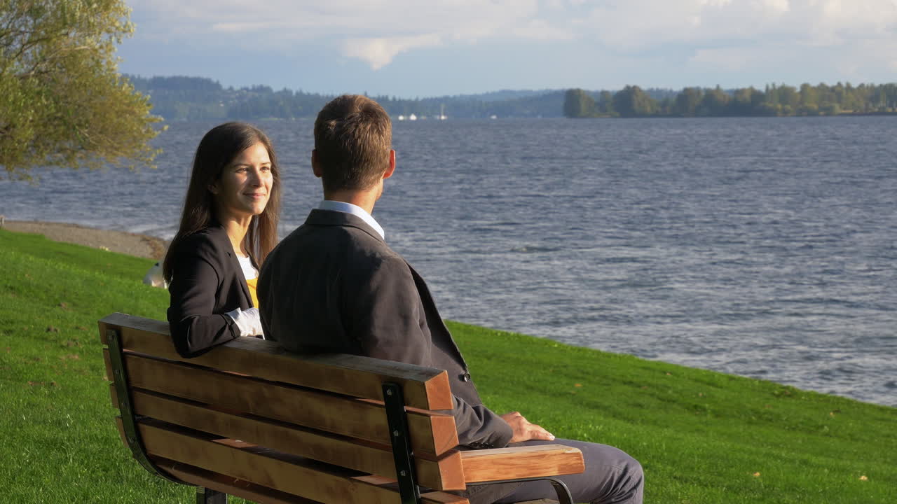 Business colleagues strategizing together on a bench in a sunny park next to a beautiful lake.
