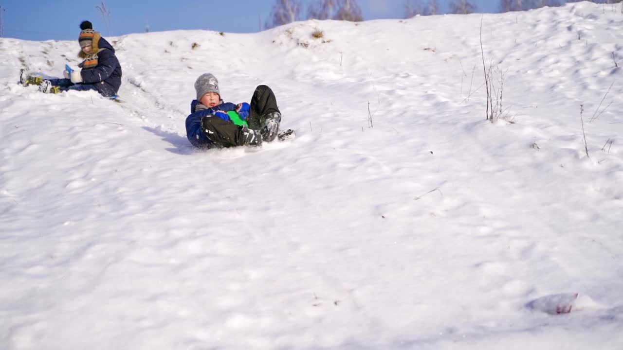 Frost winter season. Two children ride down a hill, winter games and fun. Kids laughing, sledging down a hill. Children ride down a hill, winter games and fun. Slow motion.