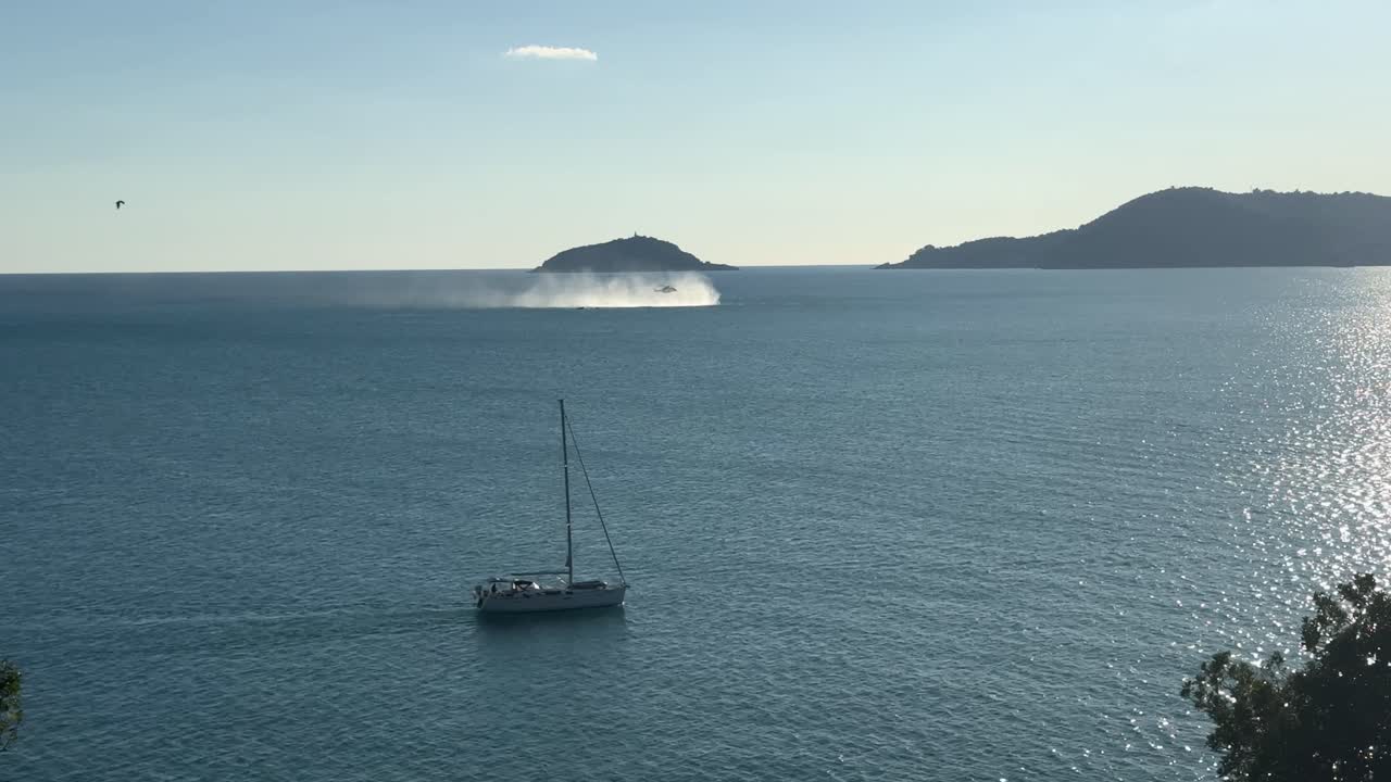 Sailboat cruising in the Ligurian Sea with helicopter spray visible near Tino Island in the background