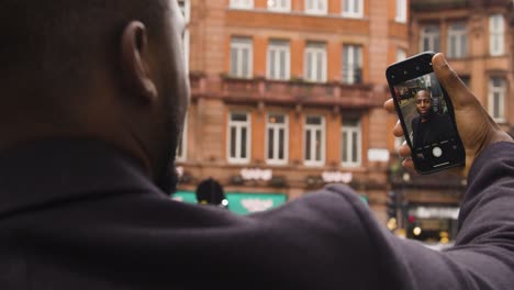 Black-male-taking-a-selfie-photo-on-his-smart-phone-on-a-street-in-London-City